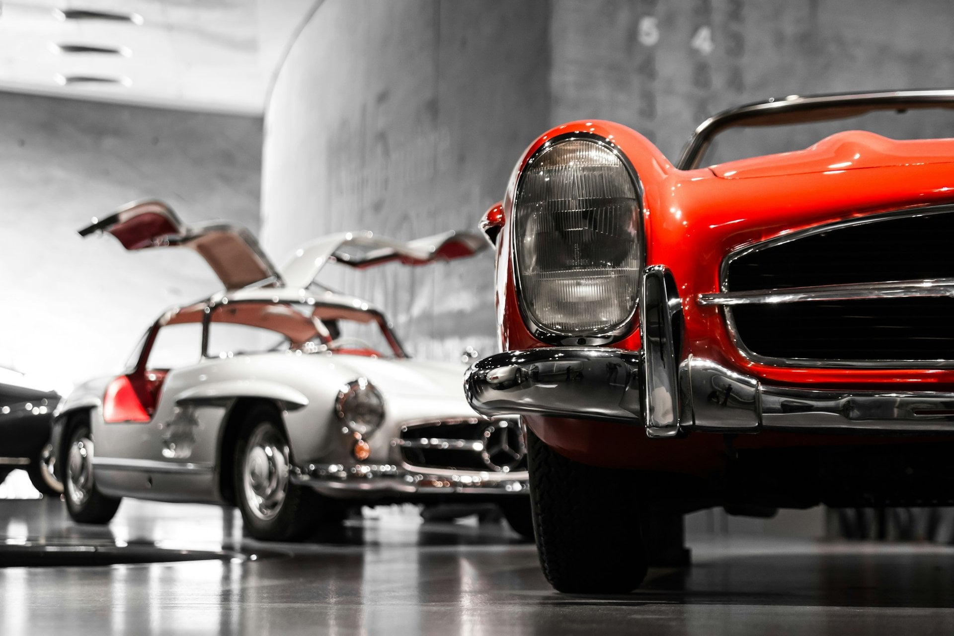 Silberner Mercedes 300 SL Flügeltürer und roter 300 SL Roadster in einer Ausstellungshalle