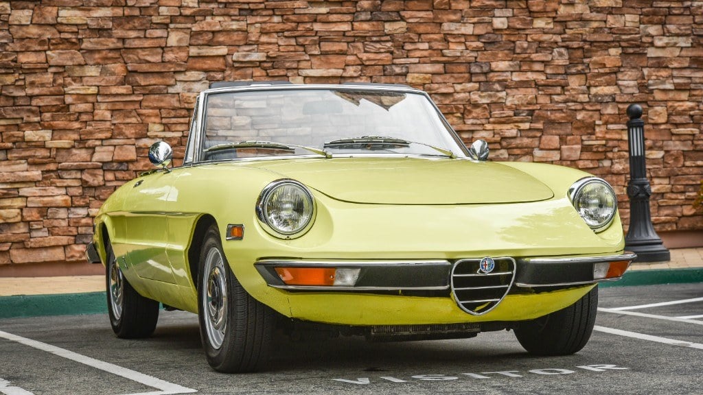 Hellgelber Alfa Romeo Spider vor einer Natursteinmauer
