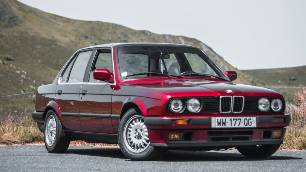 Weinrote BMW 3er Limousine (E30) vor einer Bergkulisse