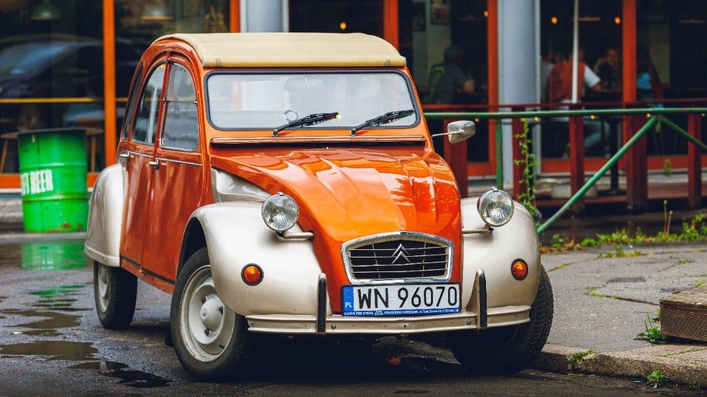 Orange-beiger Citroën 2CV am Strassenrand vor einem Lokal