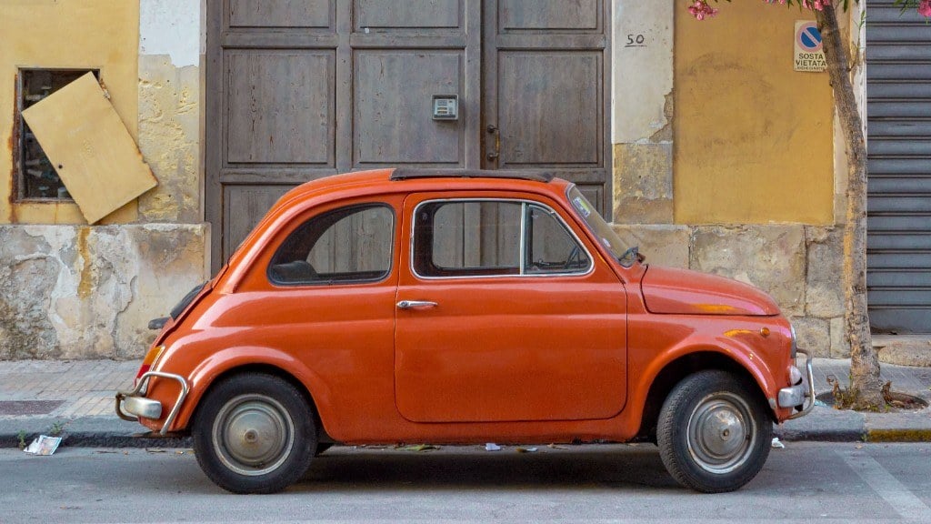 Roter Fiat Nuova 500 in der Seitenansicht vor einer Altstadtfassade