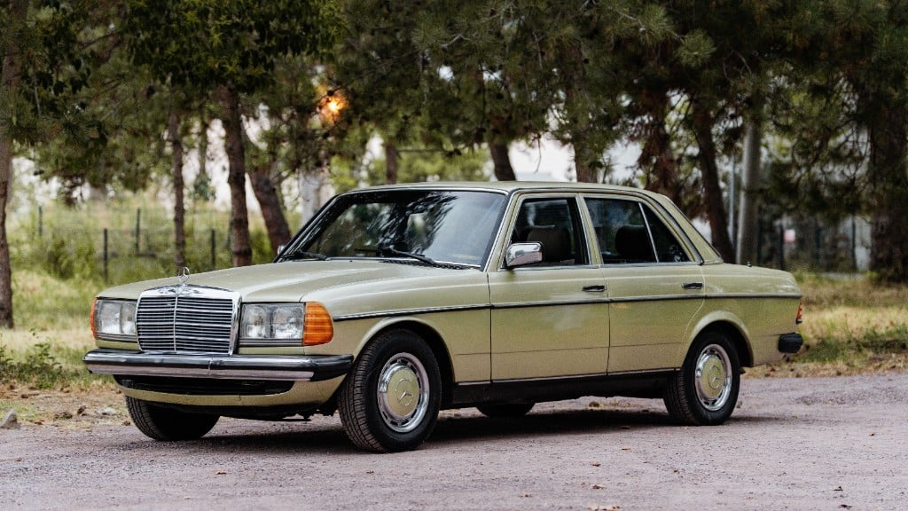 Hellgrüne Mercedes-Benz W123 Limousine auf einem Kiesplatz vor Bäumen