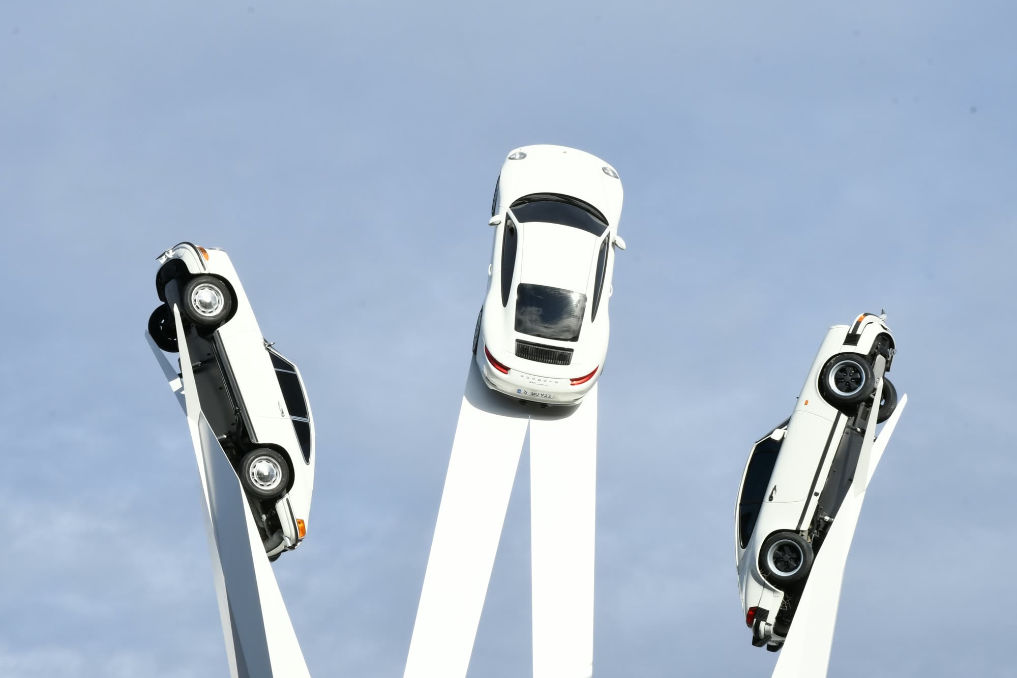 Skulptur Inspiration 911 mit drei weissen Porsche 911 auf hohen Stelen vor blauem Himmel