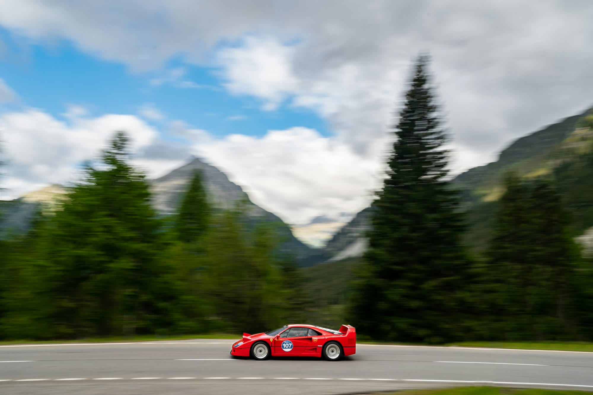 Ferrari F40 rossa con numero di gara su una strada presso St. Moritz, abeti e montagne sullo sfondo