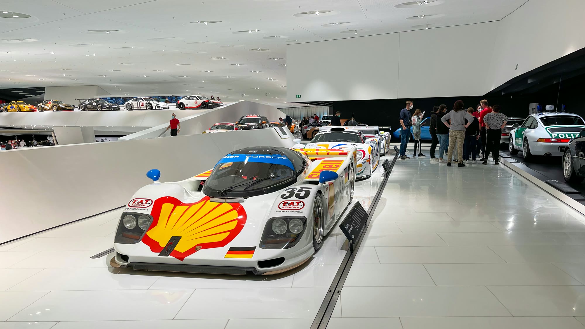 White exhibition hall of the Porsche-Museum with endurance racing cars and visitors