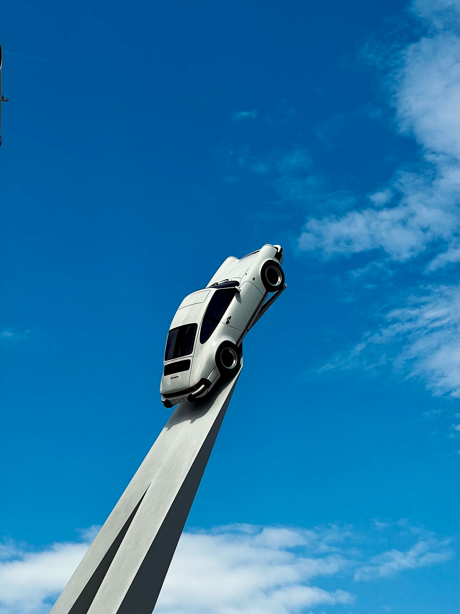 White Porsche 911 on a slanted stele against a blue sky with clouds