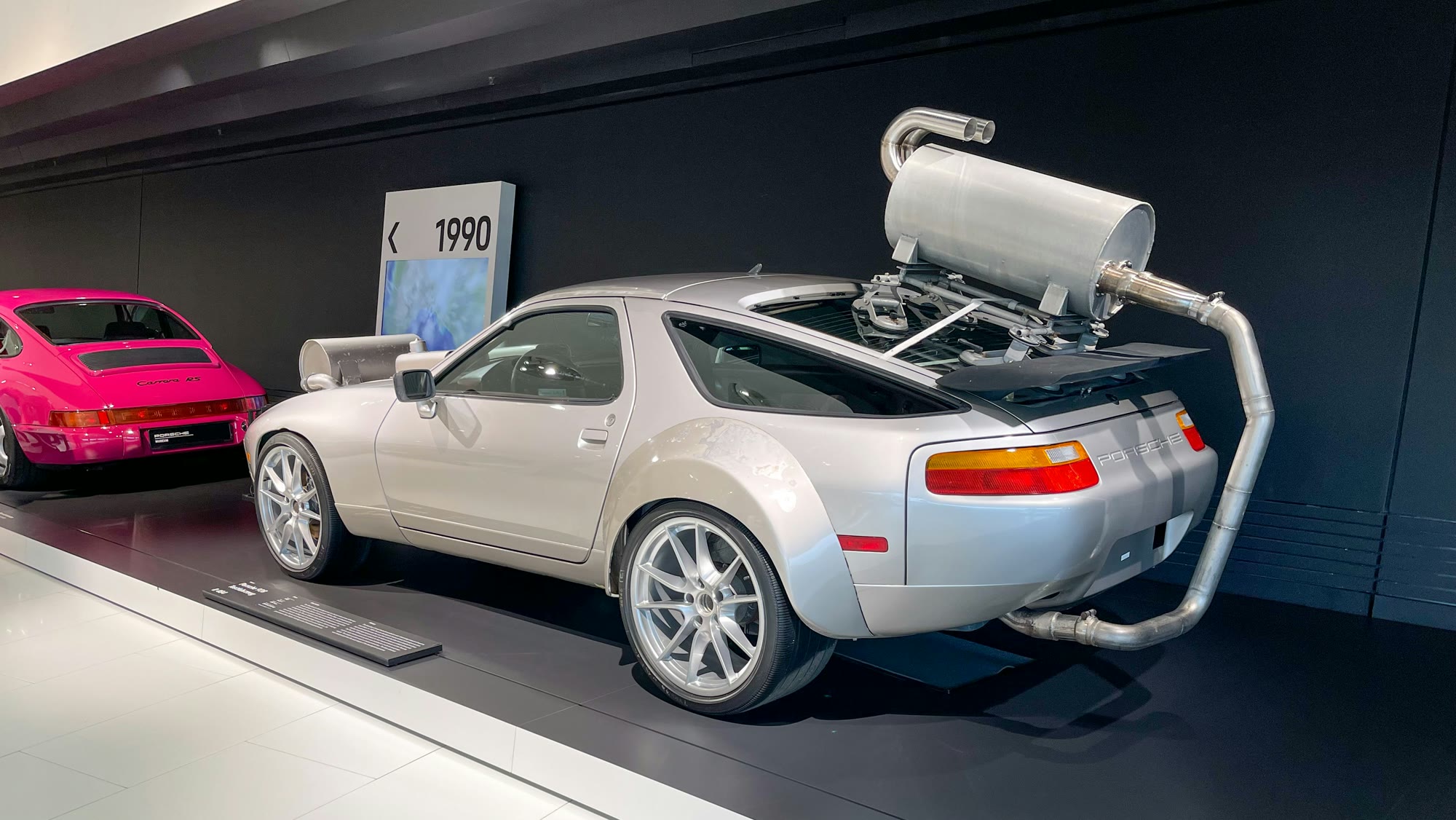 Silver Porsche test mule with the exhaust routed outside, a pink Porsche beside it